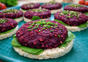 Apetyczne wegetariańskie burgery z buraka podane na waflach ryżowych ze świeżymi liśćmi szpinaku, ułożone na turkusowym talerzu. Soczyste, intensywnie bordowe kotleciki tworzą kolorową i zdrową przekąskę dla dzieci.