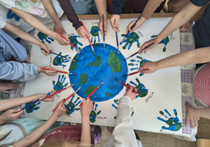 „Dzieci wspólnie malują planetę Ziemię i odbijają kolorowe dłonie na dużym arkuszu papieru.”