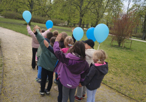 dzieci na ścieżce odwrócone plecami trzymające niebieskie balony