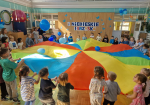 dzieci na sali gimnastycznej trzymające kolorową chustę KLANZA na której odbijają cię niebieskie balony
